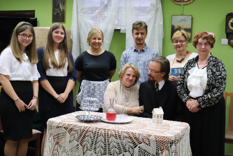 Uczestnicy Narodowego Czytania w Miejskiej Bibliotece Publicznej w Mławie: z przodu dwie osoby siedzą przy stole, z tyłu sześć osób stoi.