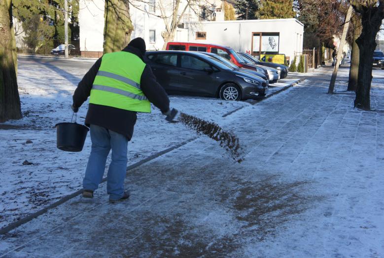 mężczyzna posypujący piaskiem chodnik