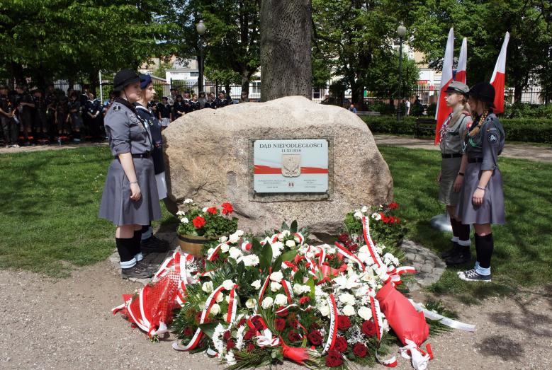 głaz przy Dębie Niepodległości, obok: harcerze, przed: wiązanki kwiatów