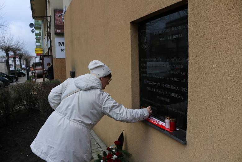 kobieta kładąca znicz przy tablicy pamiątkowej