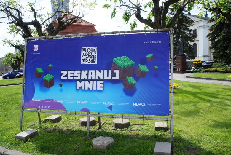 Baner w stylistyce gry Minecraft z napisem ZESKANUJ MNIE i kodem QR nad napisem, na niebieskim tle