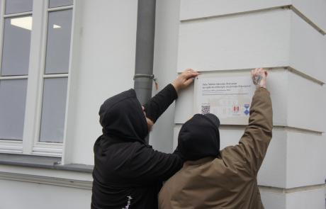 Dwaj mężczyźni montujący tabliczkę na elewacji Pałacu Ślubów