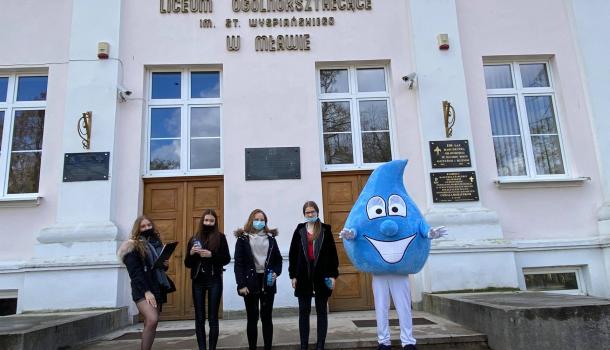 Cztery uczennice i żywa maskotka kropli wody przed budynkiem szkoły