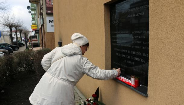 Uczestniczka uroczystości stawia zapalony znicz